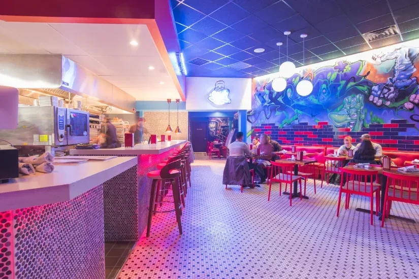 Modern restaurant with neon lighting, open kitchen, and colorful graffiti mural.