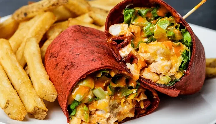 Red tortilla chicken wrap halves with orange sauce and fries.