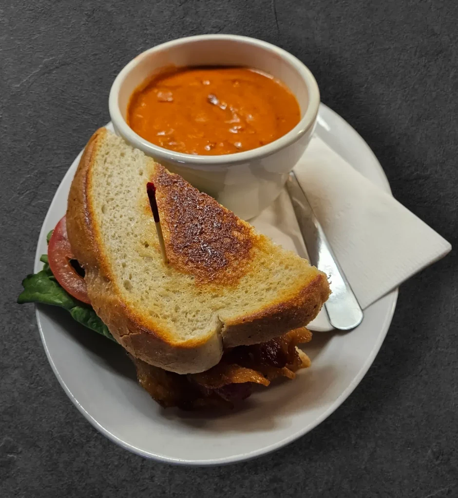 Grilled BLT sandwich and tomato soup on a white plate.