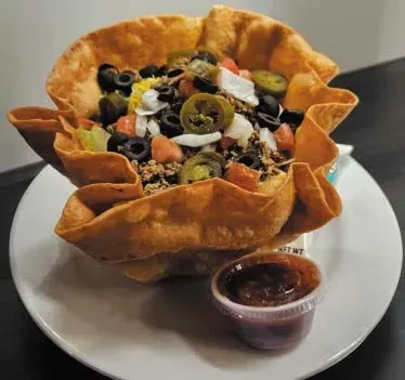 Taco salad in a crispy tortilla bowl with meat, vegetables, and salsa.