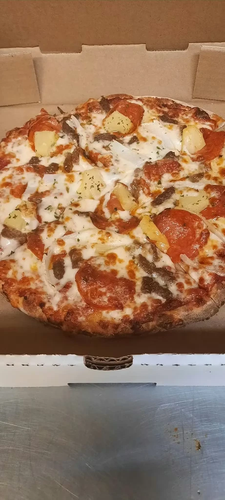 Close-up pizza with cheese, pepperoni, pineapple, sausage, onion in box.