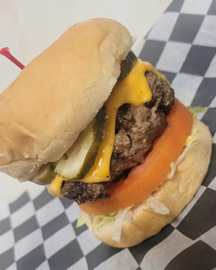 Tilted close-up of classic cheeseburger with melted cheese, lettuce, tomato, pickles.