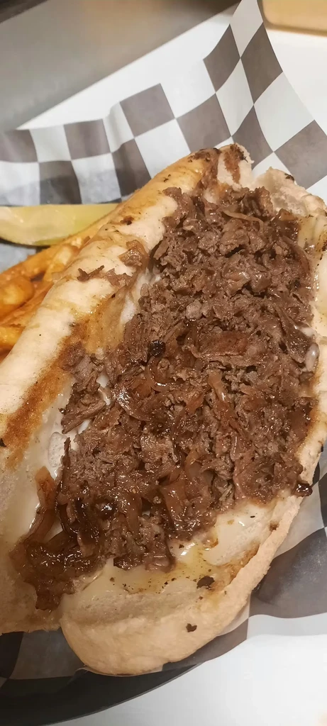 Close-up cheesesteak sandwich with melted cheese, onions, fries, and pickle.