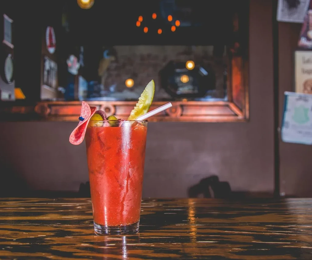 Bloody Mary cocktail with pickle, olives, and salami on a dark table.