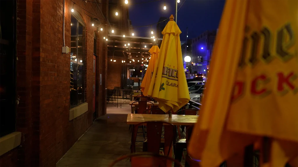 Empty urban restaurant patio at night with string lights and yellow umbrellas.