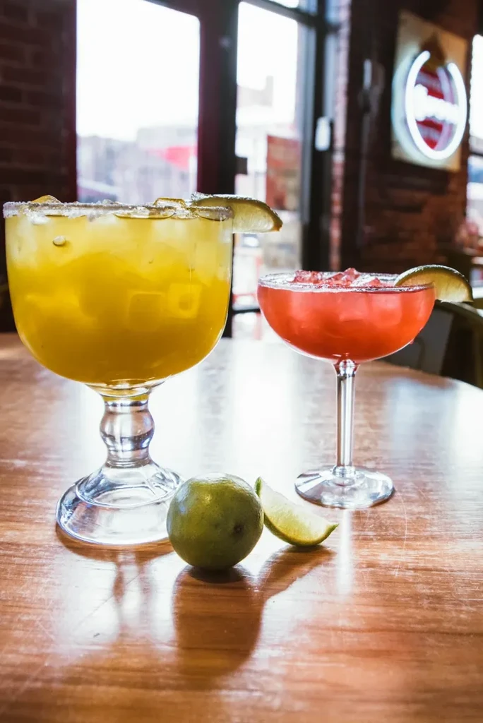 Yellow and pink cocktails with lime garnishes on a wooden table.