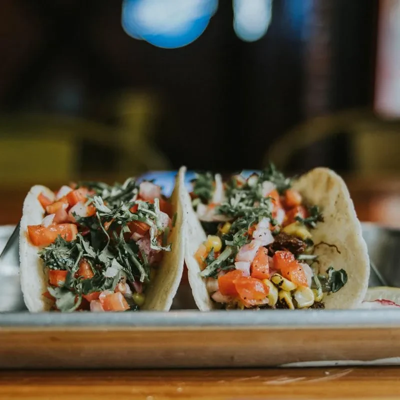 Two colorful tacos with tomatoes, corn, and cilantro on a tray.
