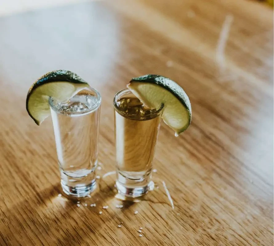 Two tequila shots, clear and amber, with lime and salt.