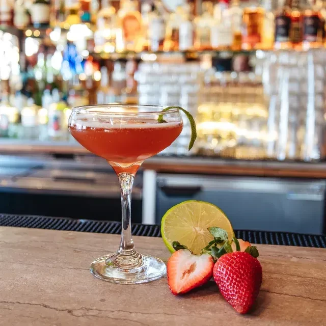 Reddish cocktail, lime, strawberries on a stone bar top.