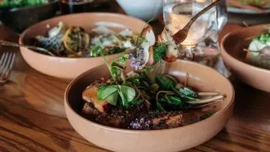 Beautifully plated meat dish with herbs and edible flowers on a table.