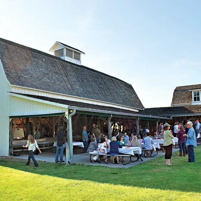 White barn and covered patio bustling with people on a sunny day.