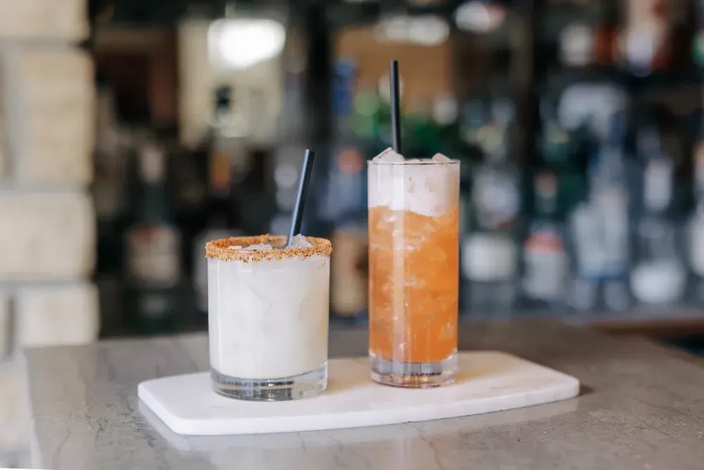 Two cocktails: white with garnished rim, amber with foam layer.