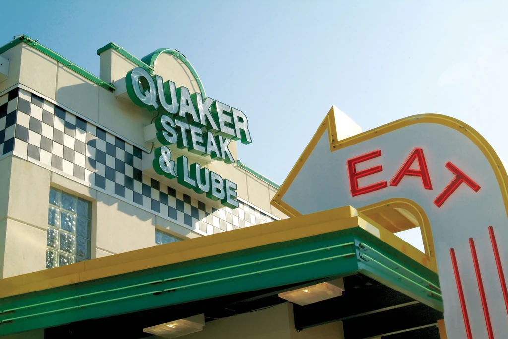 Retro Quaker Steak & Lube restaurant exterior with green neon and "EAT" sign.