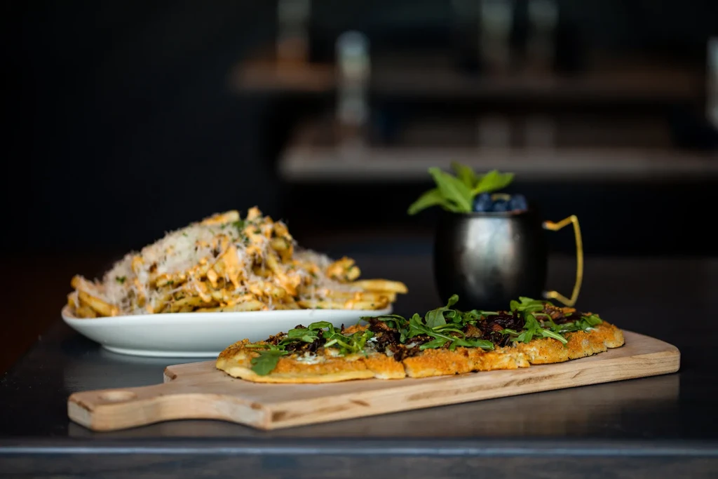 Flatbread, cheesy fries, and a mint blueberry drink on a dark surface.