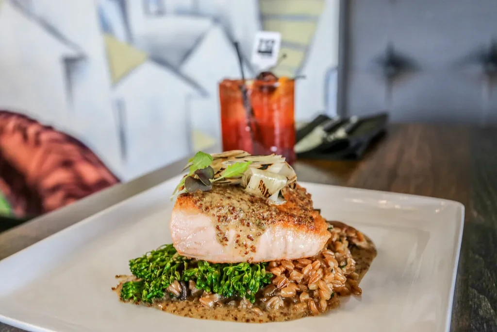 Plated salmon, creamy sauce, microgreens, and grains on white plate.