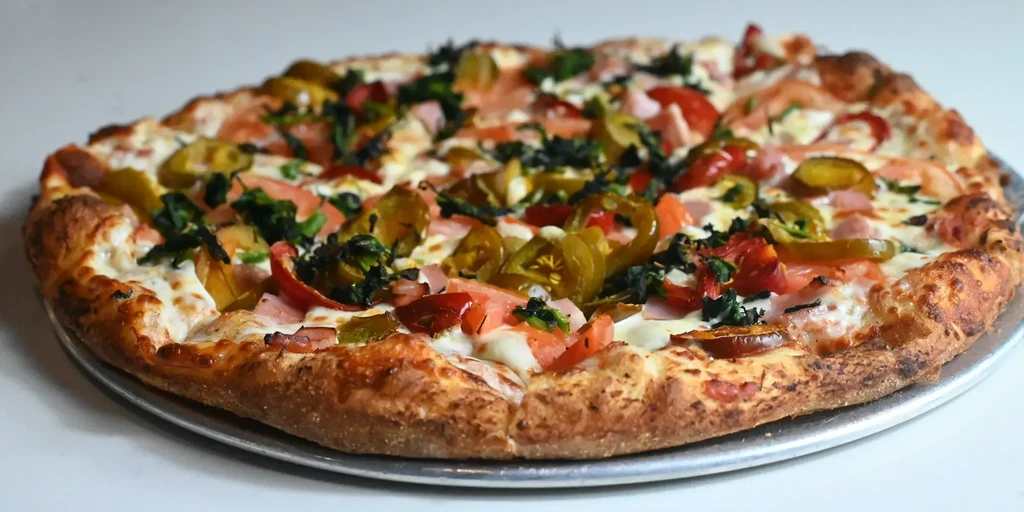 Baked pizza with golden crust, melted cheese, tomatoes, jalapeños, and greens.