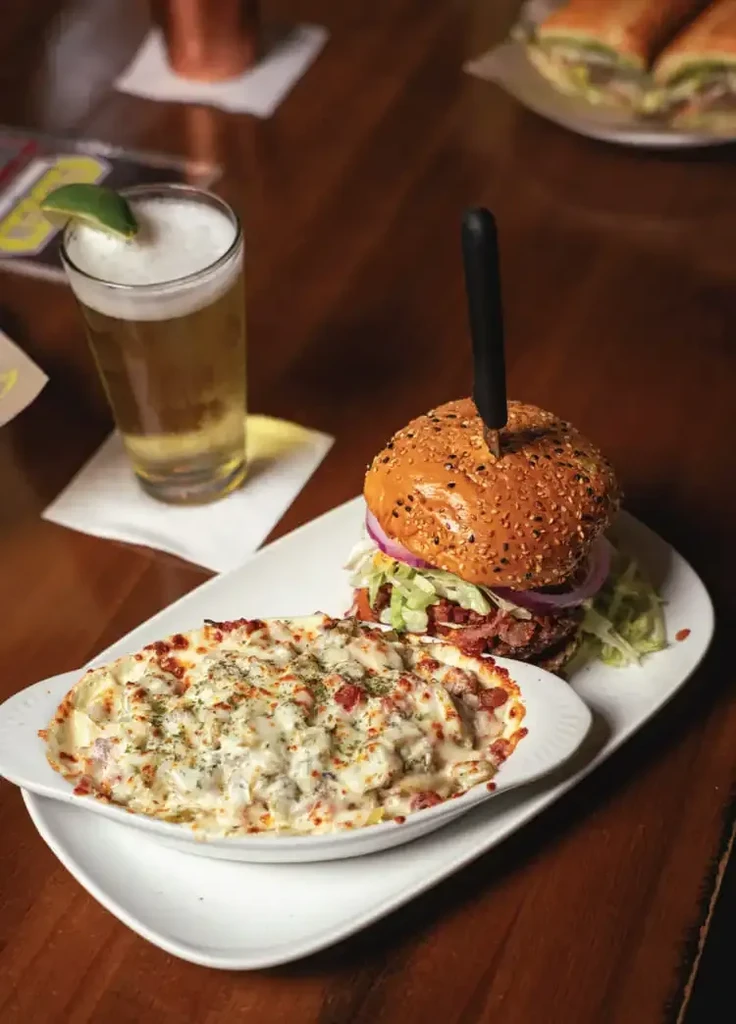 A burger, creamy mac and cheese, and beer on a table.