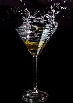 Clear liquid splashes from a martini glass with an olive against black.