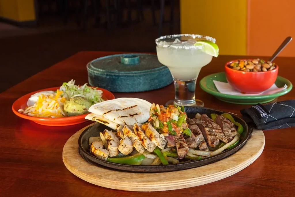 Sizzling chicken and steak fajitas with sides and a margarita.