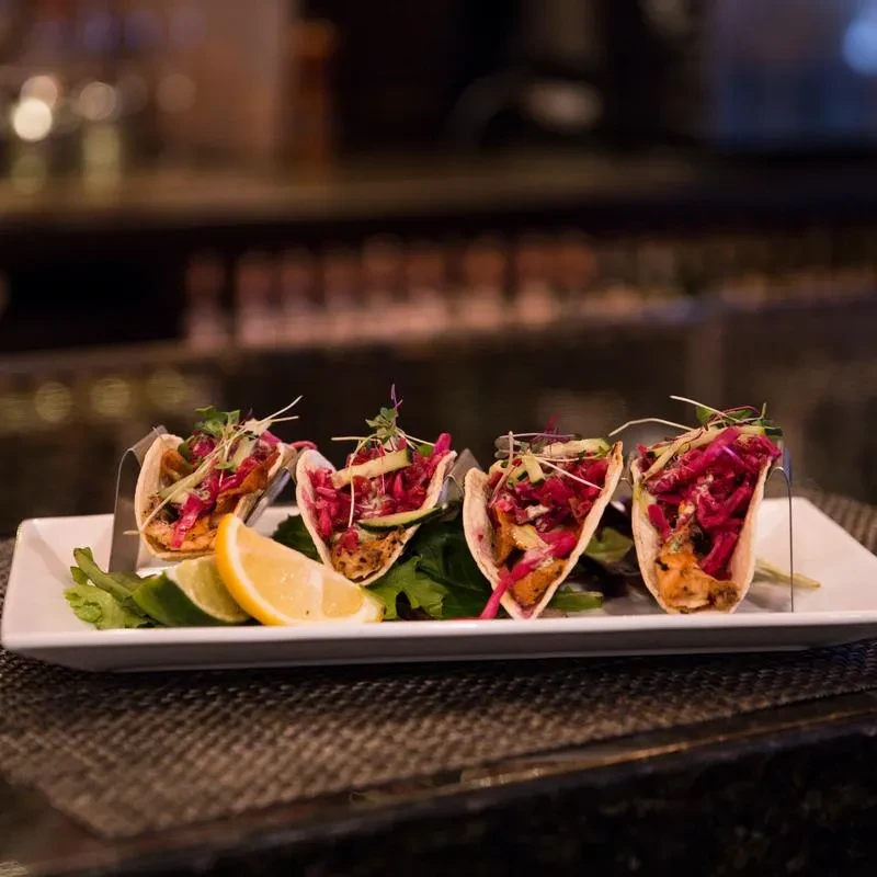 Four vibrant tacos with colorful fillings, lemon, and lime.