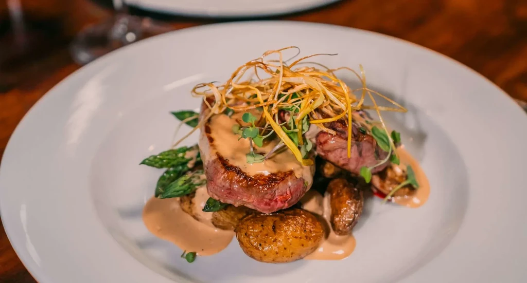 Gourmet seared steak with creamy sauce, potatoes, asparagus, and elegant garnishes.