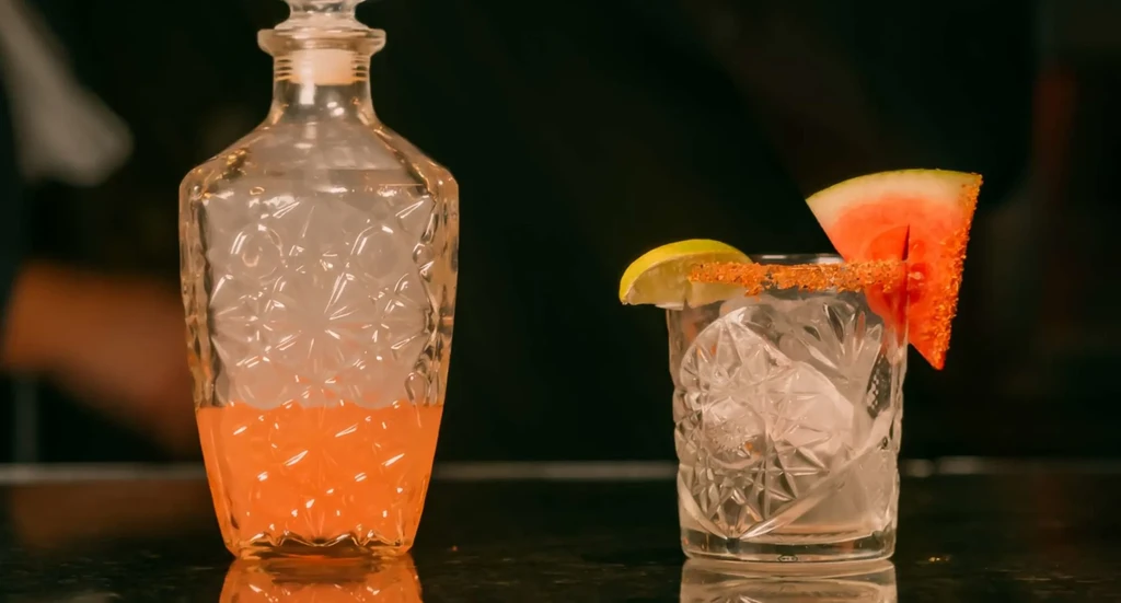 Ornate decanter with mist and ornate cocktail with fruit and ice.