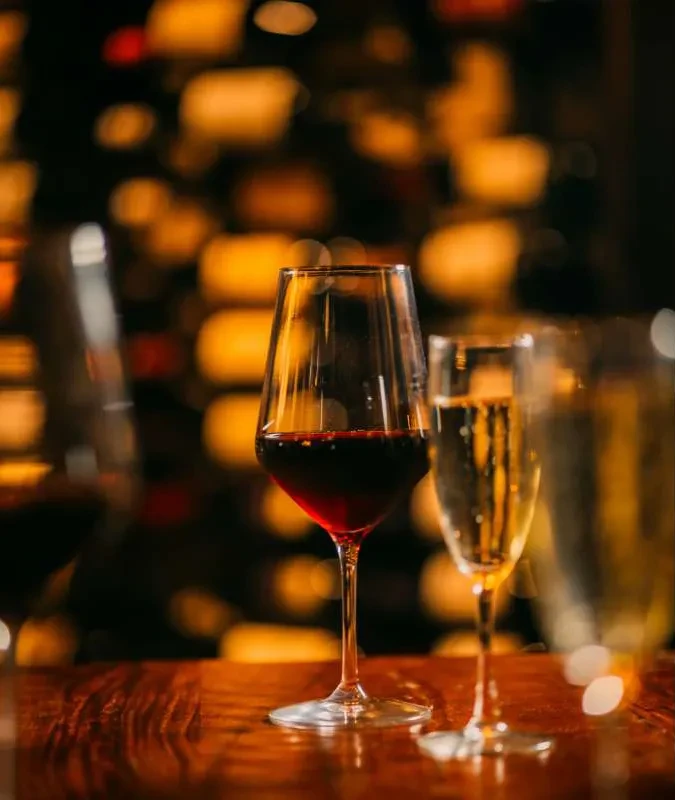 Glasses of red and sparkling wine on wood, blurred bottle background.