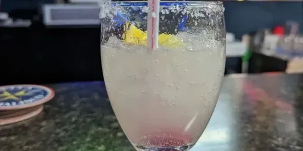 Chilled cocktail with crushed ice, pink layer, straw, and fruit garnish.