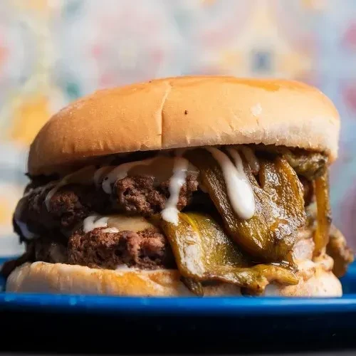 Burger with double patties, melted cheese, roasted green chiles on blue plate.