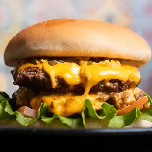 Close-up of a double cheeseburger with melted cheese, pickles, lettuce, tomatoes.