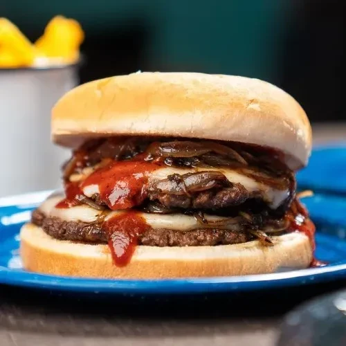 Large double-patty burger on blue plate with fries.