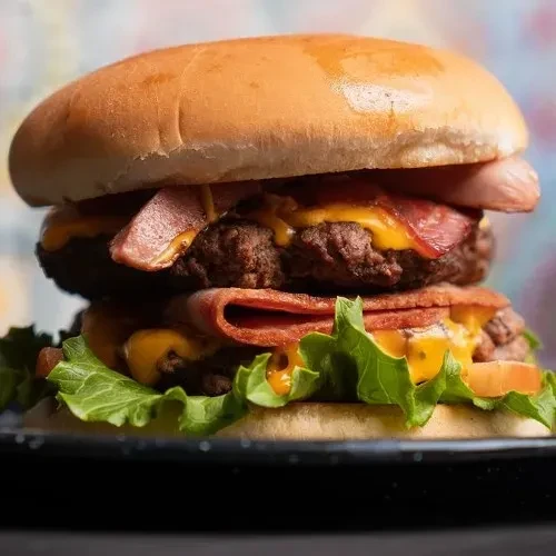 Stacked double-patty burger with bacon, sausage, cheese, and vegetables.