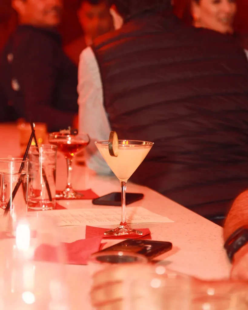 Light cocktail in martini glass, other drinks, blurred bar patrons.