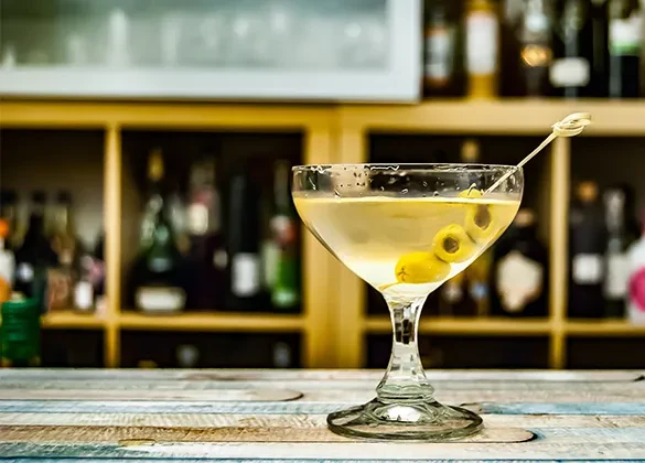 A cold martini with yellow liquid and three olives at a bar.