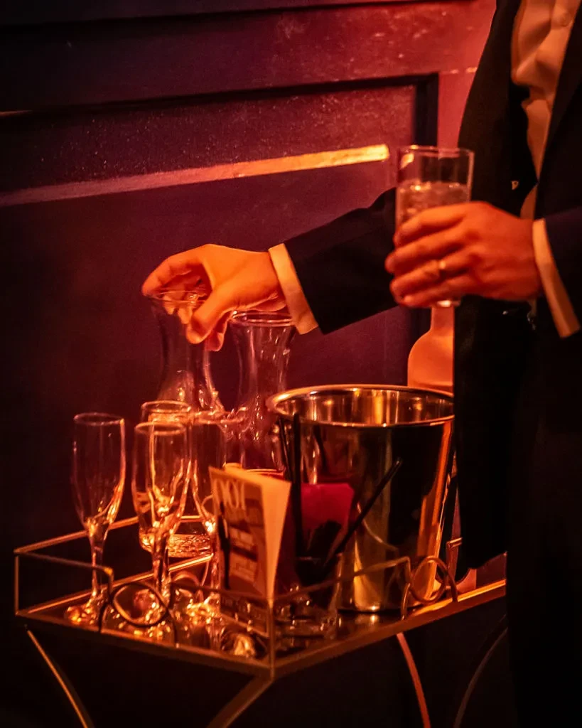 Person in dark suit prepares drinks on elegant golden bar cart.