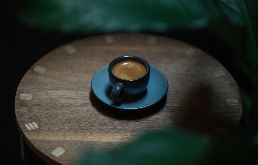 Dark ceramic espresso cup with crema on a wooden table.