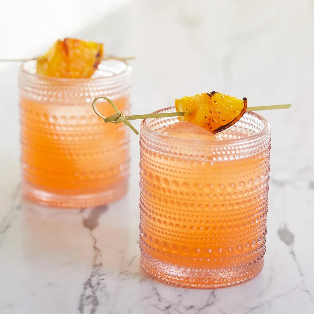 Two peach cocktails in textured glasses with charred orange slices.