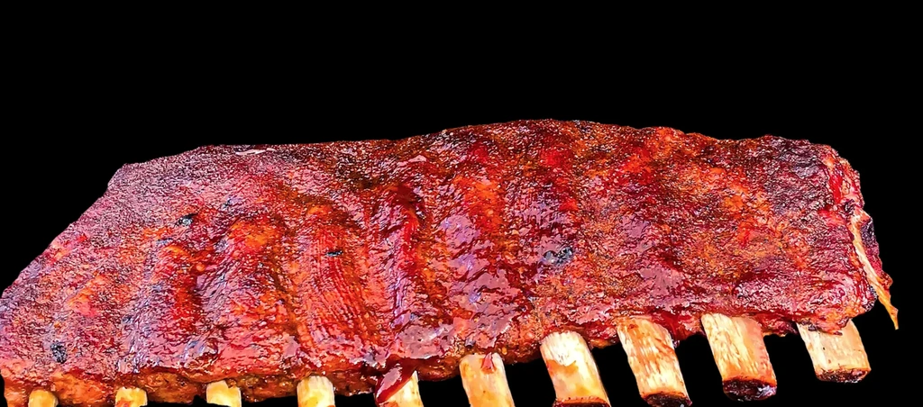 Full rack of glossy, charred BBQ ribs on a black background.
