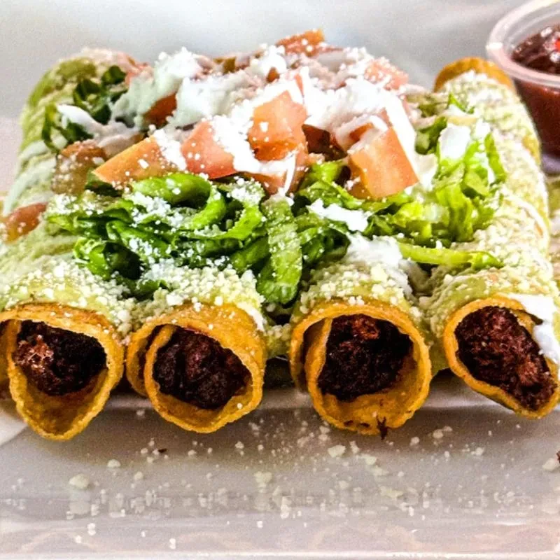 Four fried taquitos topped with green sauce, lettuce, tomatoes, and cheese.