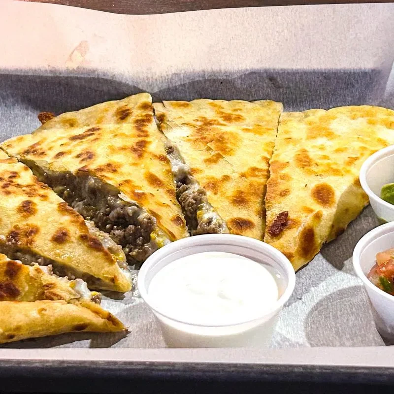 Quesadilla with meat and cheese, cut into triangles, with two dips.