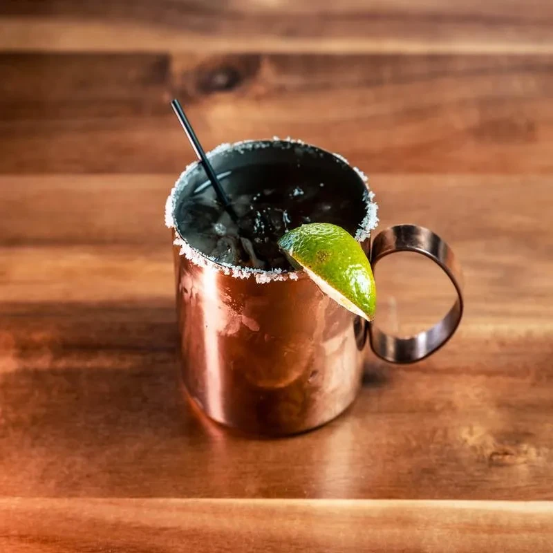 Copper mug with dark drink, white rimmed, lime, straw, ice.