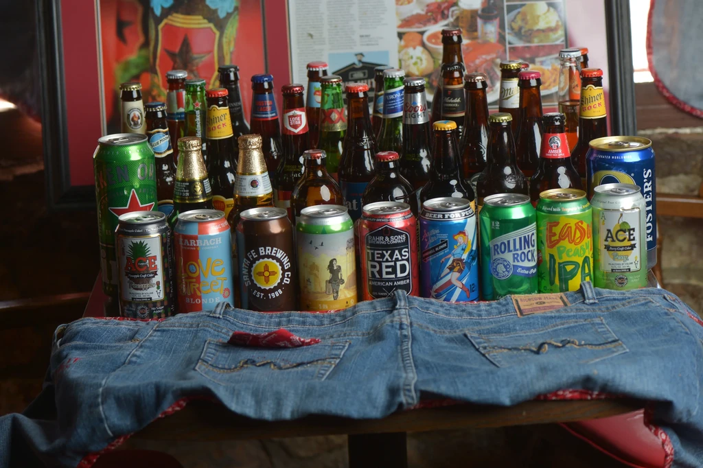 Collection of beer bottles, cans, and jeans on a wooden surface.