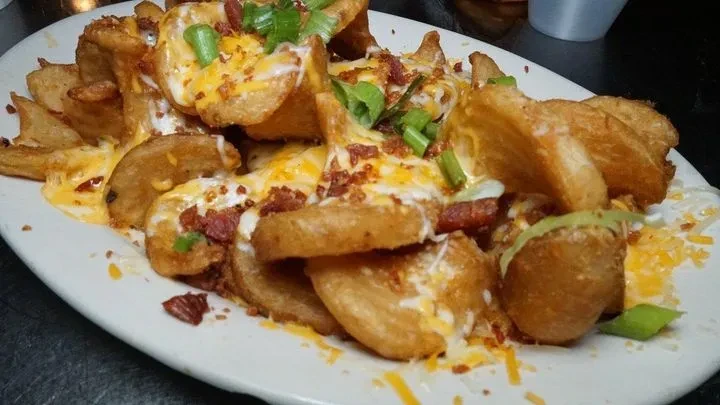 Loaded potato wedges topped with cheese, bacon, green onions, and creamy sauce.
