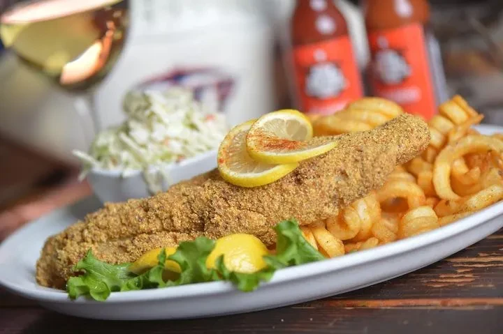 Golden fried fish fillet, curly fries, lemon, coleslaw on plate.
