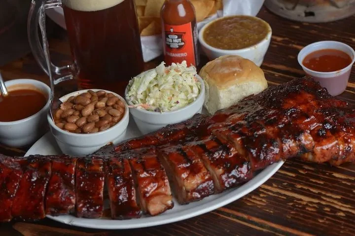 Pre-sliced glazed BBQ ribs with sides, beer, and hot sauce.