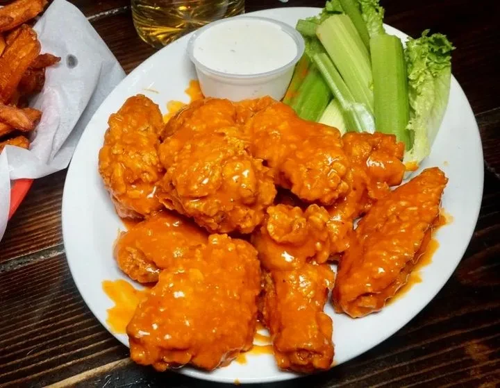 Plate of glossy buffalo wings with celery, dip, fries, and beer.