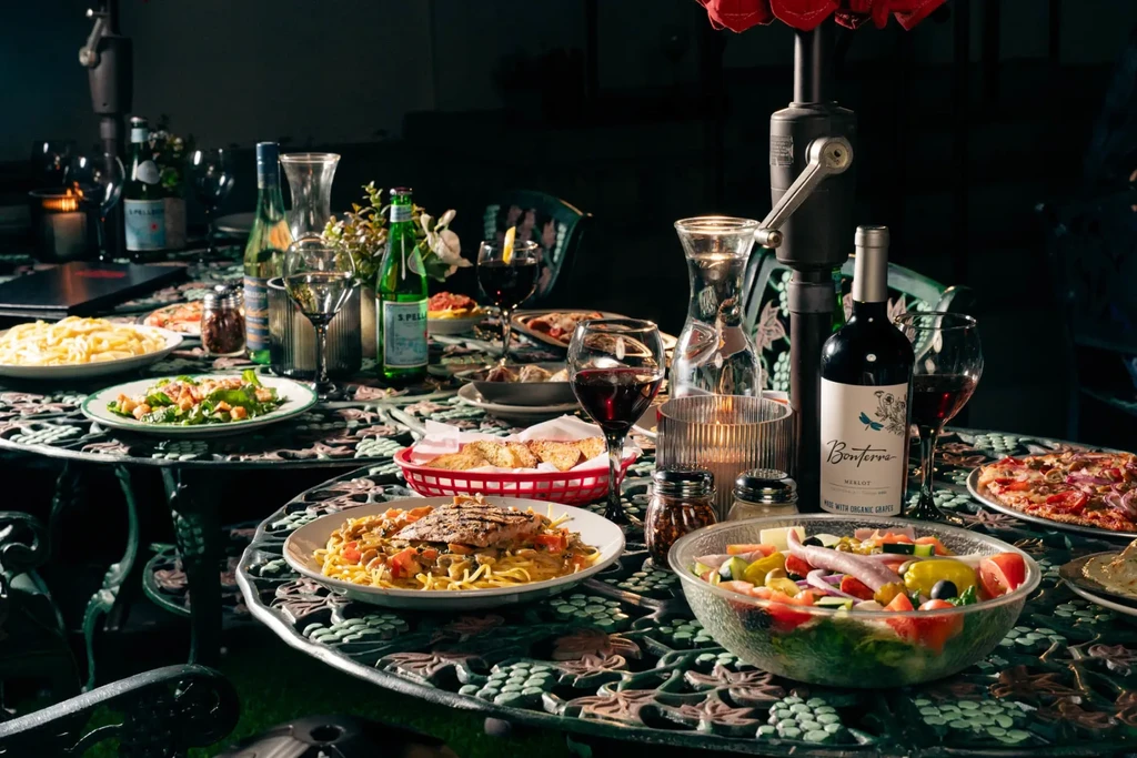 Outdoor table filled with Italian dishes, wine, water, and candles.