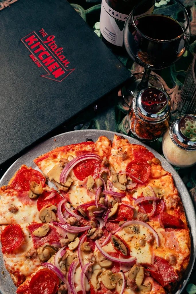 Sliced pizza with pepperoni, mushrooms, wine, menu, and shakers.