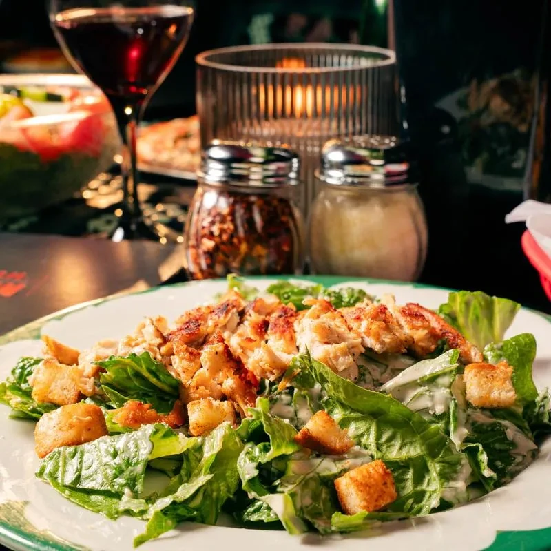 Well-lit Caesar salad with grilled chicken, croutons, red wine, and a lit candle.