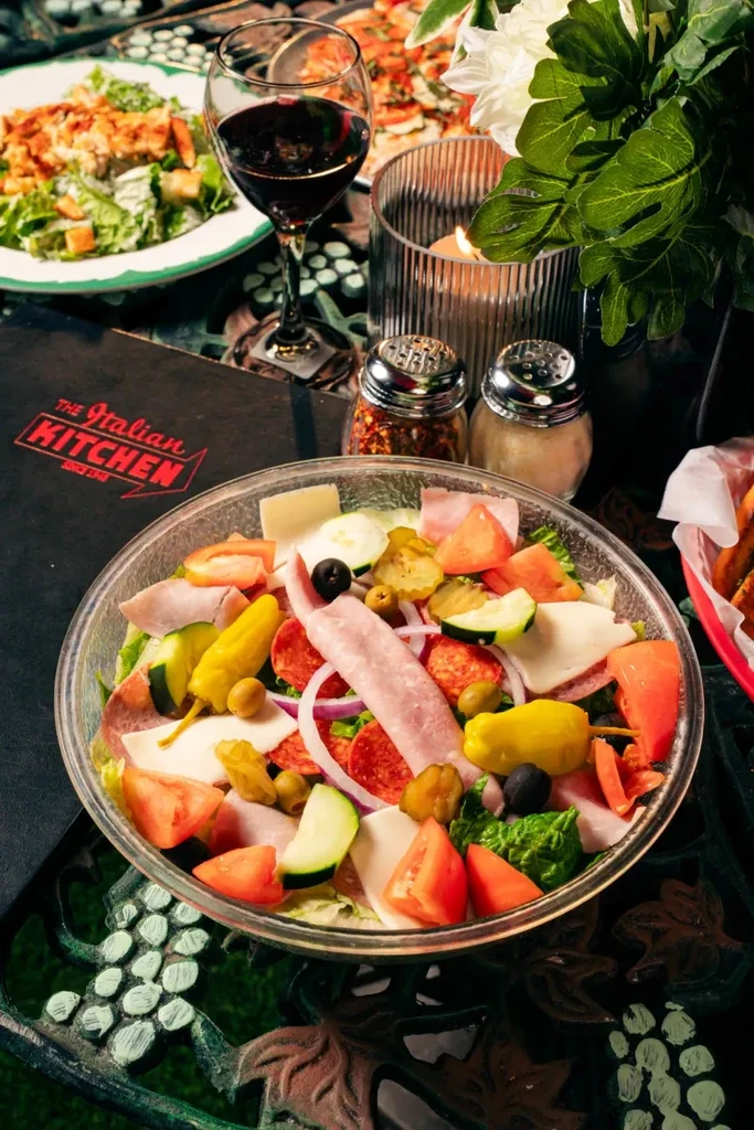 Vibrant Italian antipasto salad, wine, and pizza on restaurant table.